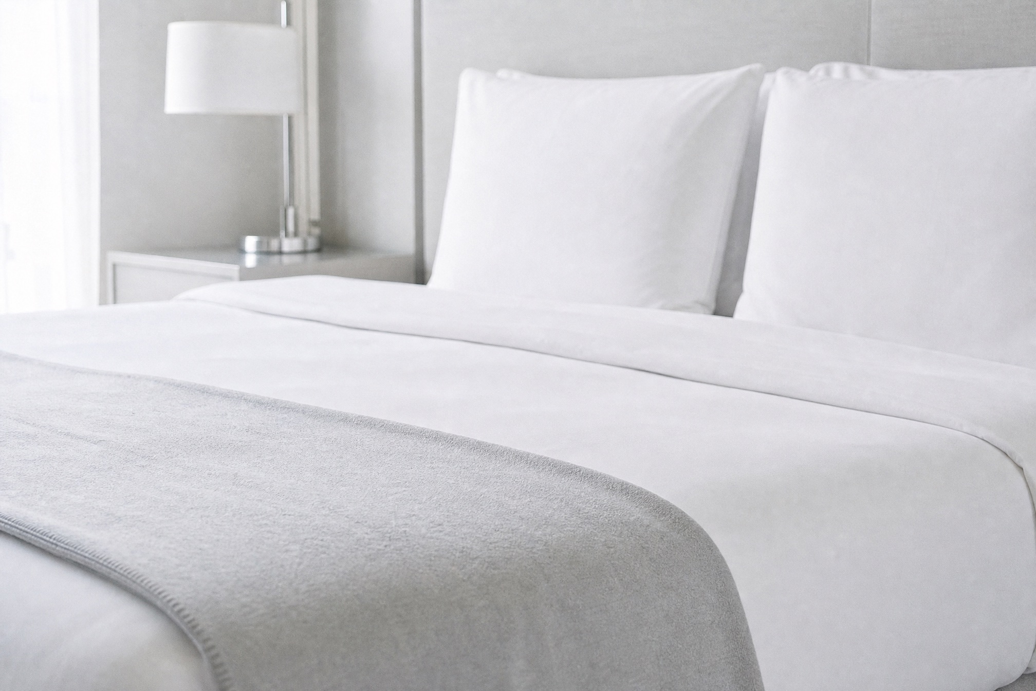 Frisch bezogenes Hotelbett mit weißer Bettwäsche, aufgeschüttelten Kissen und gefalteter Decke am Fußende